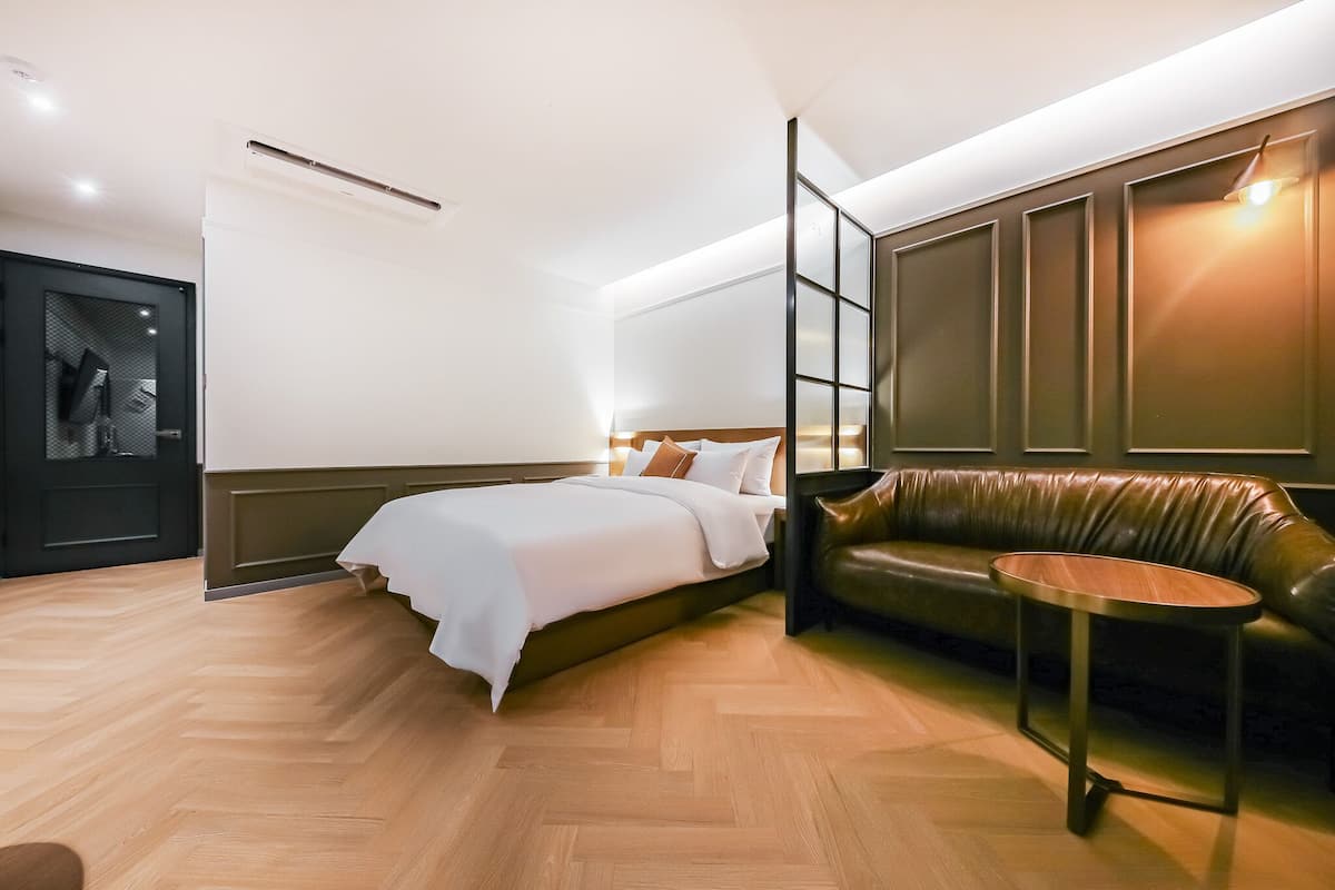 A modern hotel room with a bed, a leather sofa, a small table, and a wardrobe.