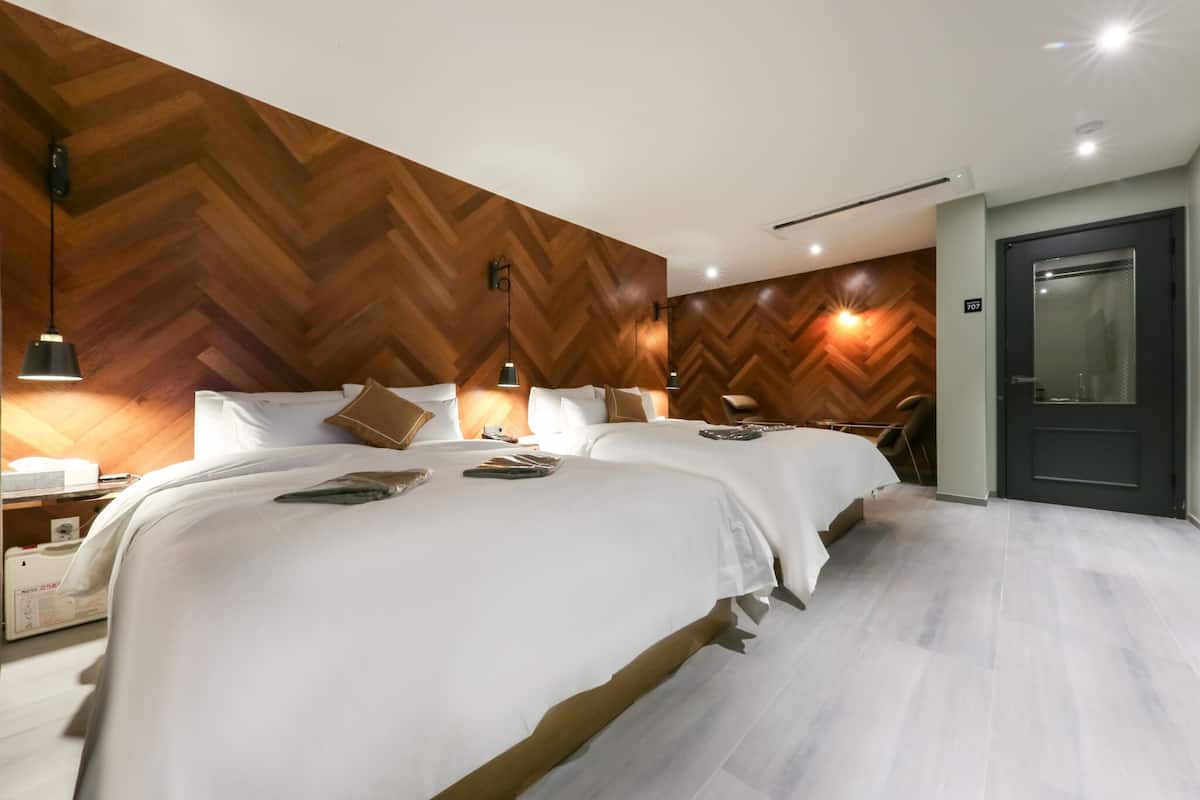 A hotel room with two beds, wooden panel walls, a dark door, and a light-colored floor.