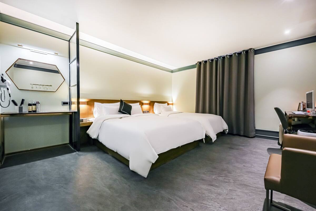 A hotel room with a large bed, a desk with a chair, a mirror, and a window with curtains.