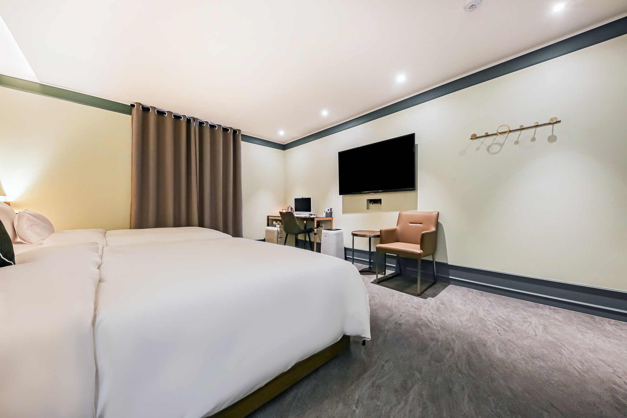 Habitación de hotel con una cama grande, un escritorio con silla, un televisor montado en la pared y un perchero con ganchos.