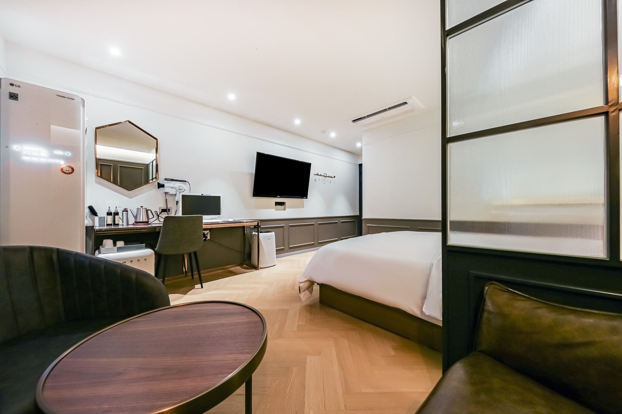 A hotel room with a bed, a desk with a chair, a TV, a mirror, and a window with blinds.