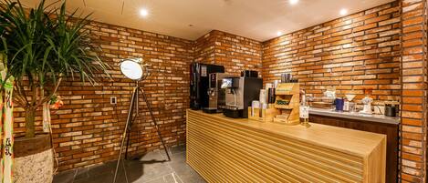 A reception area with a brick wall, a wooden reception desk, a coffee machine, and a potted plant.