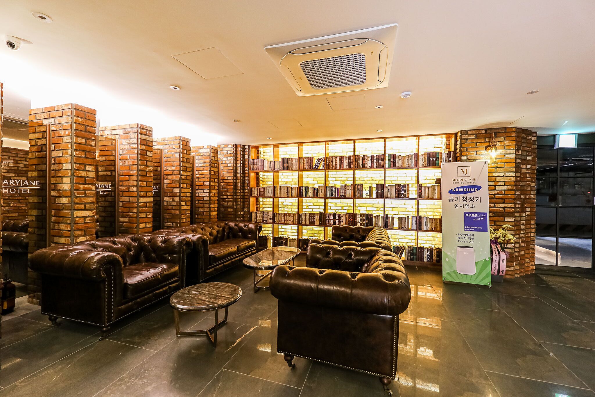 A lobby with leather sofas, a brick wall bookshelf, and a Samsung advertisement.