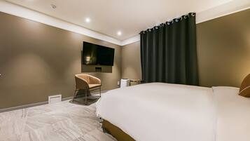 A modern hotel room with a large bed, a flat-screen TV mounted on the wall, a chair, and a small table.