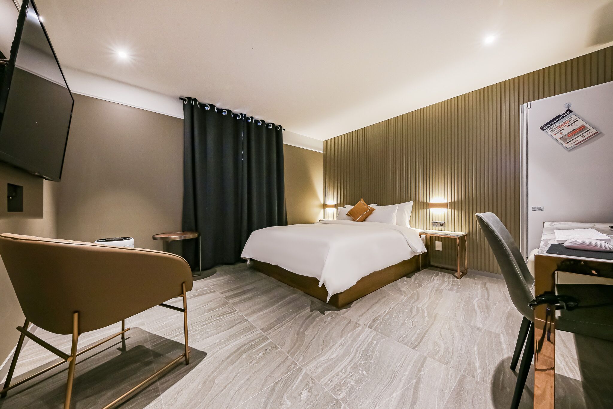 A hotel room with a bed, a desk, a chair, a TV, and a wall-mounted bulletin board.
