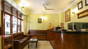 A reception area with a wooden reception desk, a brown leather sofa, a small table with magazines, and a ceiling fan. - Siddhartha Hotel Sundhara (Kathmandu)