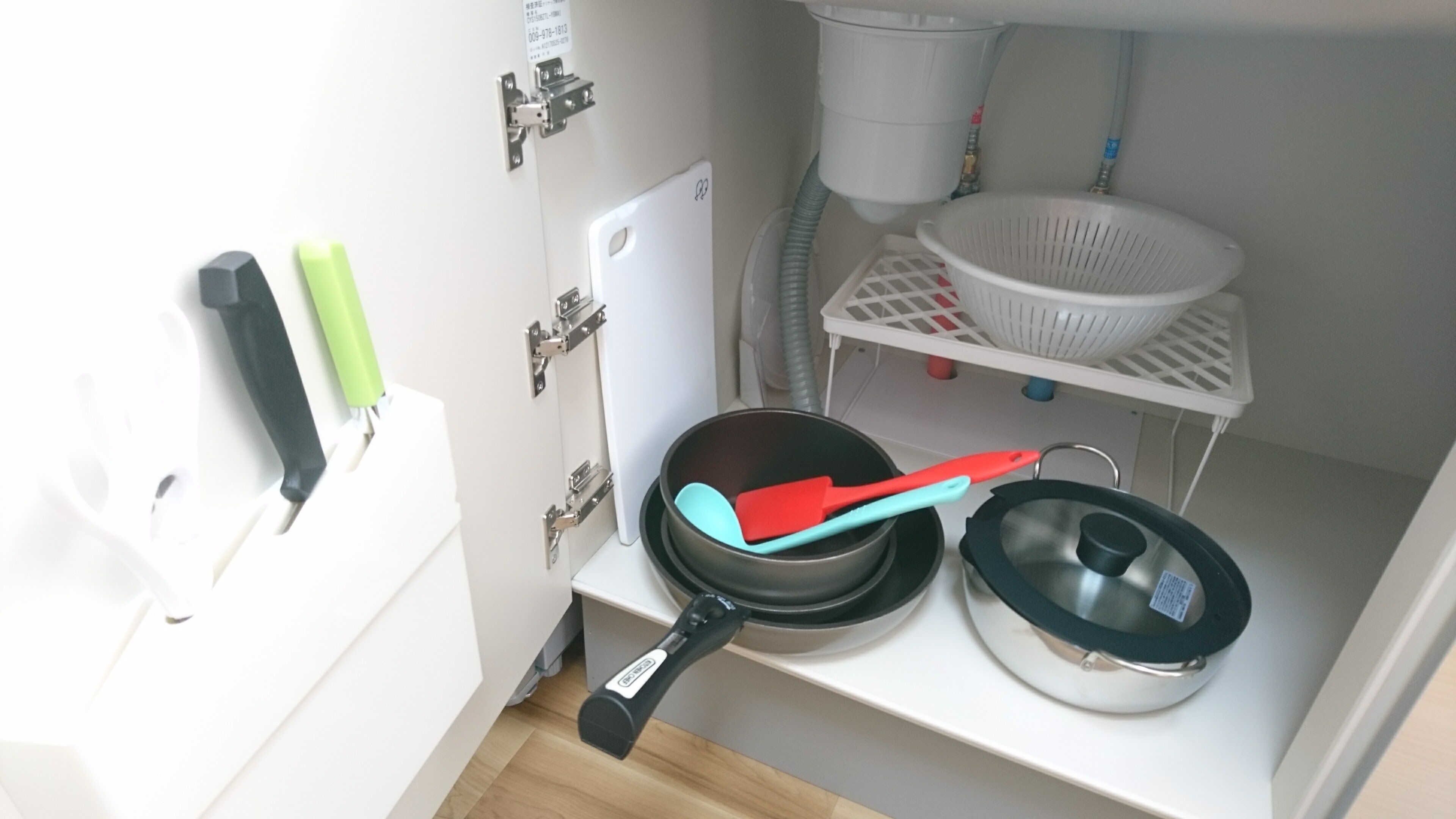 Een keuken met een wit aanrecht, een zwarte koekenpan met rode spatel, een witte zeef en een wit apparaat.