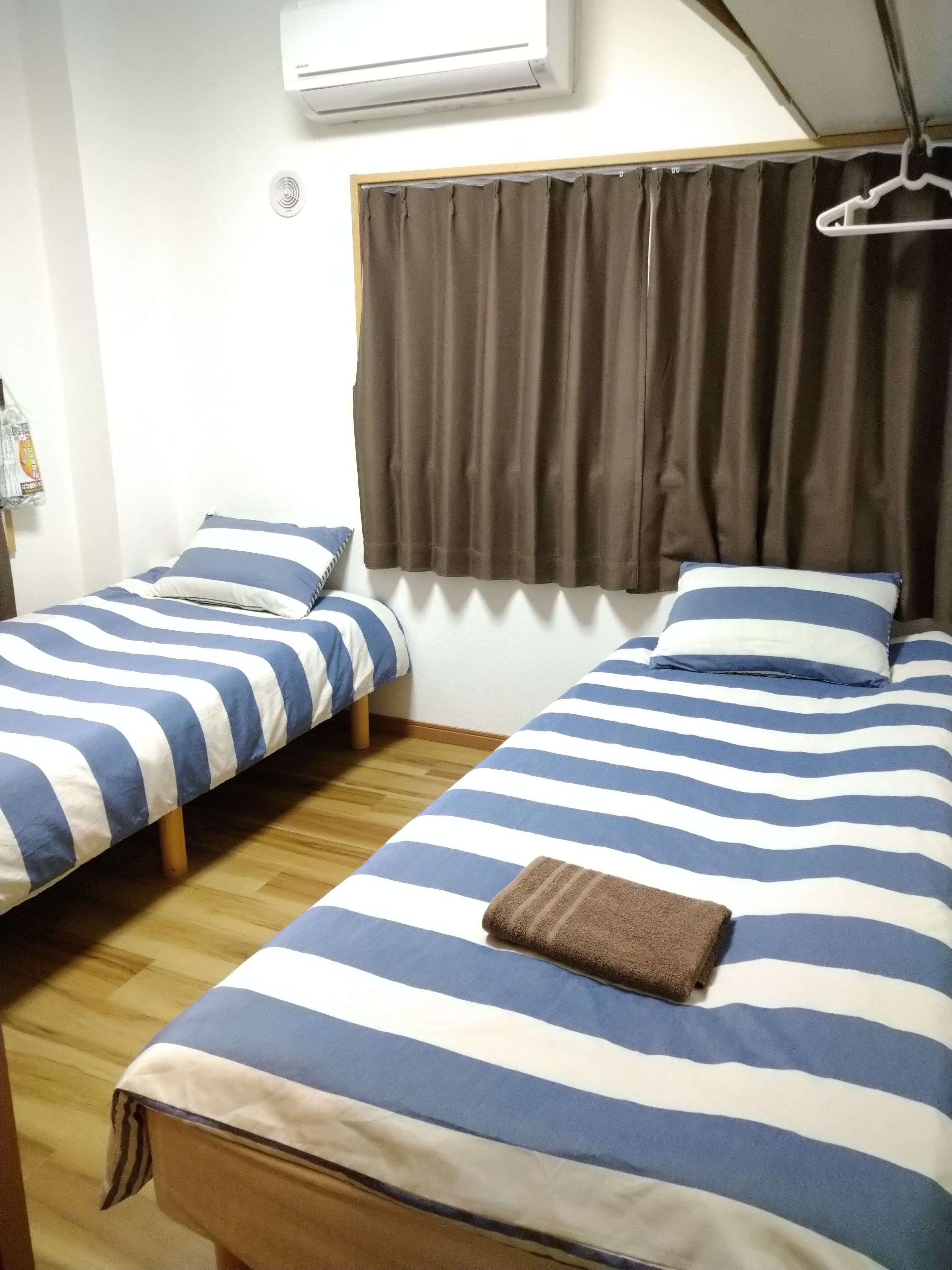 A room with two beds, each with striped bedding, a window with curtains, and an air conditioning unit on the wall.