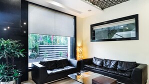 Un salón moderno con un sofá de cuero negro, una mesa de centro de vidrio y un amplio ventanal con persianas.