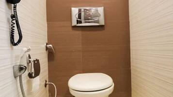 Un baño pequeño con inodoro, secamanos y teléfono.