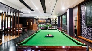 Una sala de billar con mesa de pool verde, zona de estar y bar.