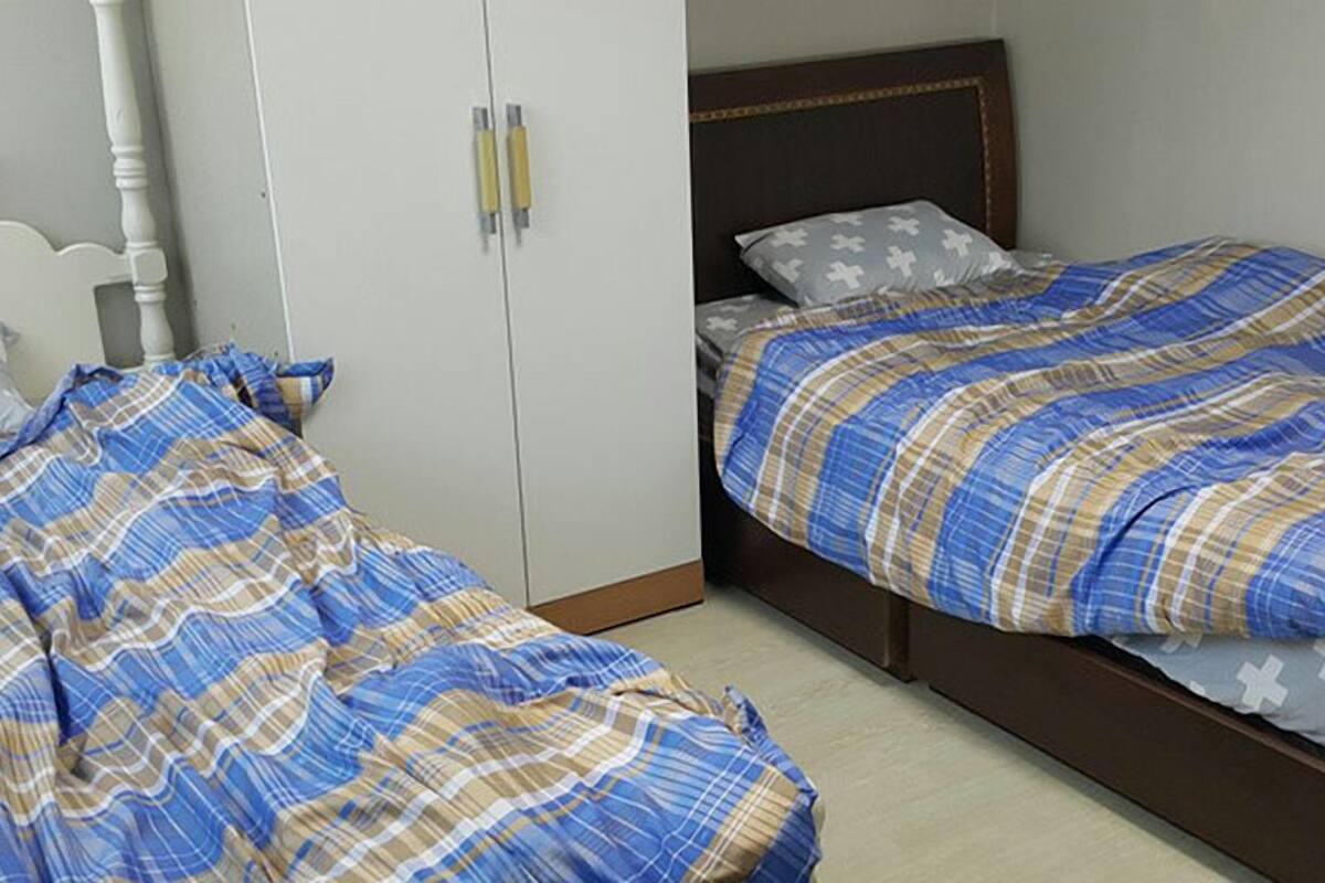 Ein Schlafzimmer mit zwei Betten, beide mit einem blau-beigen Karomuster-Zudecke. Am rechten Bett befindet sich ein weißer Kleiderschrank mit zwei Griffen und ein Holz-Kopfteil.