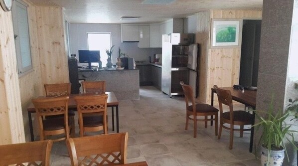 Uma sala de jantar com cadeiras de madeira e uma mesa, uma cozinha com armários e eletrodomésticos, e uma planta em vaso.