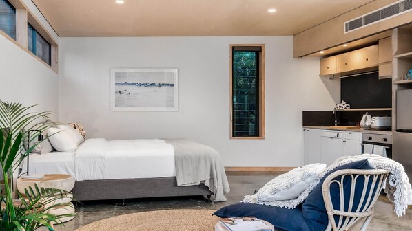 A modern bedroom with a bed, a desk, and a kitchenette.