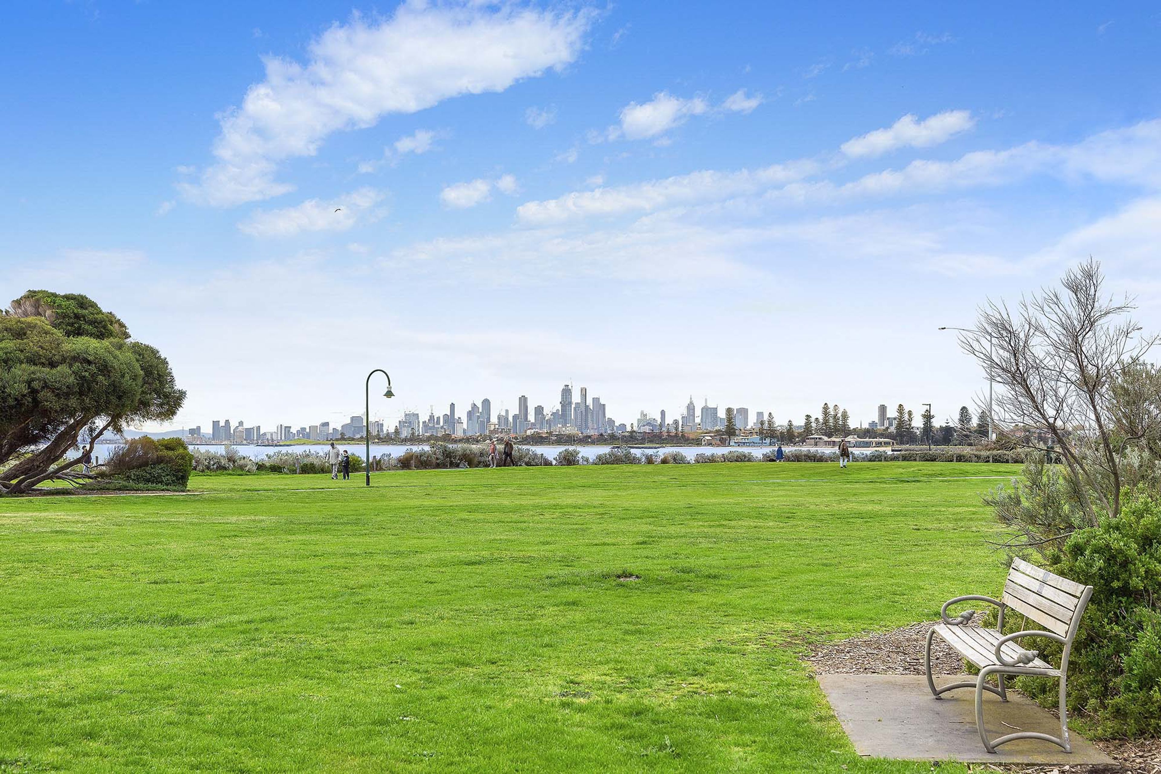 A park with a bench and a view of a city skyline across a body of water.