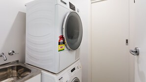 Lavanderia compacta e moderna, com máquina de lavar frontal, secadora e pia de aço inoxidável.