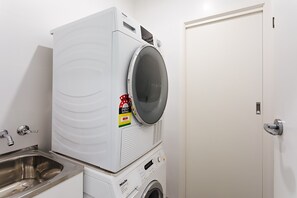 A compact, modern laundry room with a front-loading washing machine, a dryer, and a stainless steel sink. - Brighton By Sea with sea glimpses (Brighton)