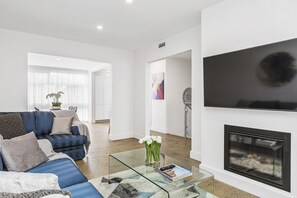 A modern living room with a blue sofa, a glass coffee table, and a fireplace.