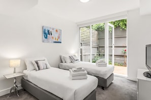 Une chambre d’hôtel avec deux lits, une télévision, un tableau et un balcon donnant sur un paysage verdoyant.