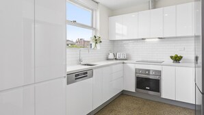 Cozinha moderna com armários brancos, lava-louças embutida, forno de aço inoxidável e janela com vista para o exterior.