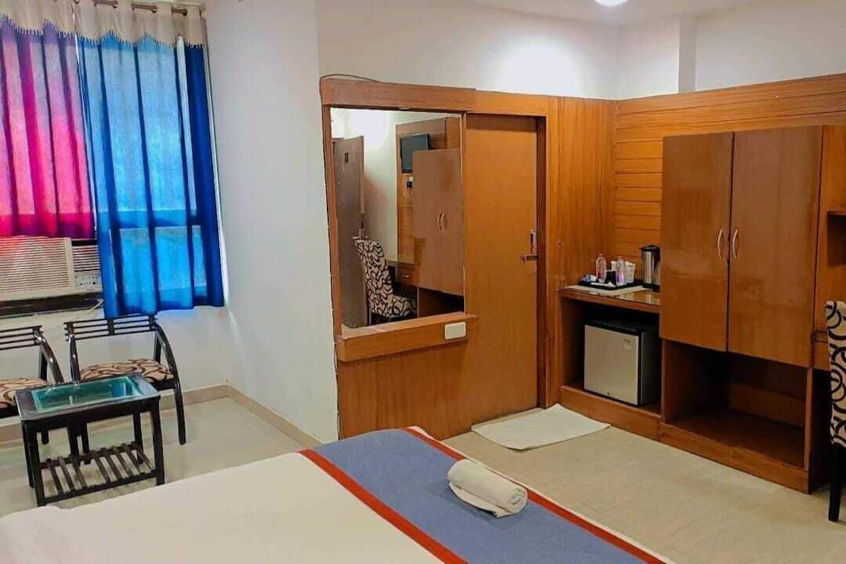 A hotel room with a bed, a desk, a chair, a wardrobe, a television, and a small table with a mirror.