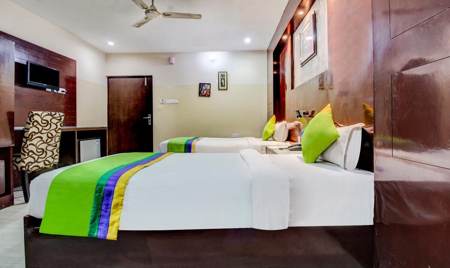 Habitación de hotel con dos camas, televisión, ventilador de techo y armario de madera.