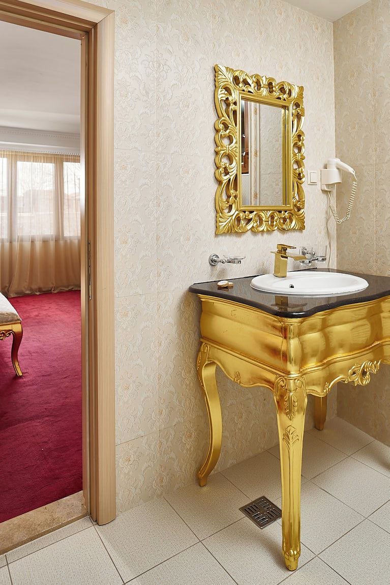 Ein Badezimmer mit goldener Waschtischgarnitur, einem großen Spiegel und einem weißen Waschbecken.