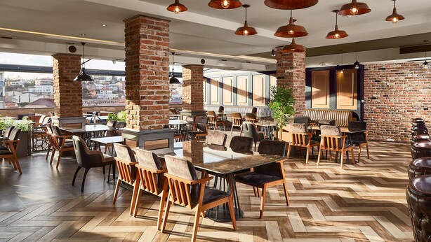 A spacious restaurant with brick columns, wooden tables, and hanging pendant lights. - Hotel Gold (Skopje)