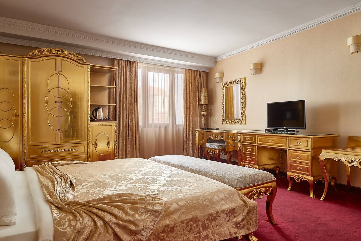 A luxurious hotel room with a large bed, a gold dresser, a television, and a desk.