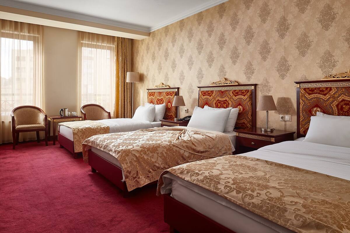 A hotel room with three beds, a desk, and a chair.