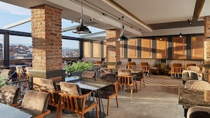 A modern restaurant with high ceilings, exposed brick columns, and large windows offering city views. - Hotel Gold (Skopje)