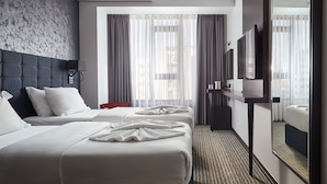 A hotel room with three beds, a dark headboard, a large mirror, and a view of the city through sheer curtains. - Hotel Gold (Skopje)