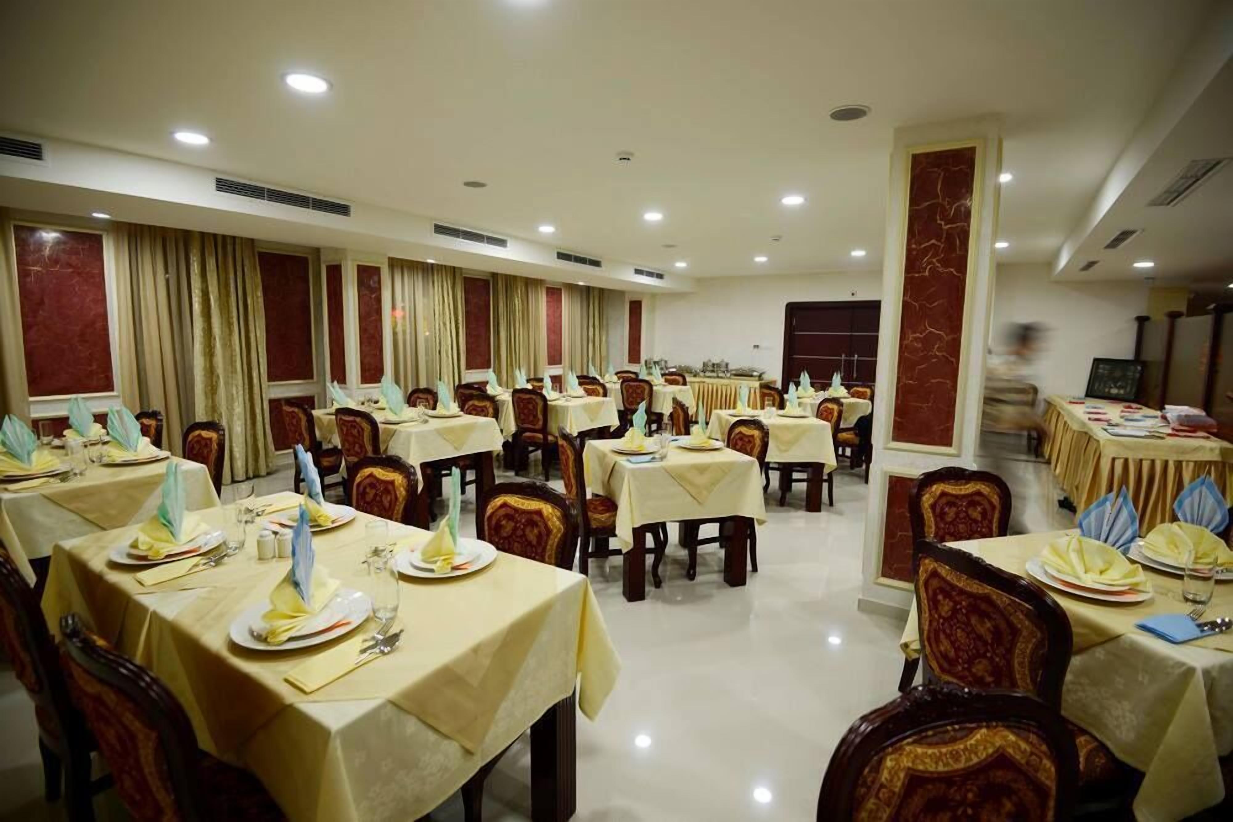 Un salón de banquetes con varias mesas dispuestas para comer, cada una con mantel, sillas y vajilla.