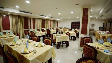 Un salón de banquetes con varias mesas dispuestas para comer, cada una con mantel, sillas y vajilla.