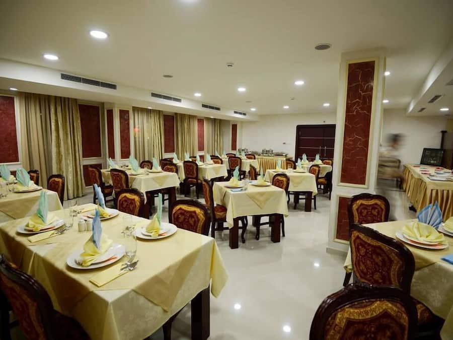 Un salón de banquetes con varias mesas dispuestas para comer, cada una con mantel, sillas y vajilla.