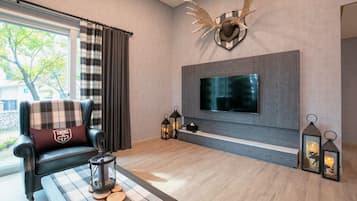 Una sala de estar moderna con un televisor de pantalla plana grande montado en una pared gris, un sofá de cuero con un cojín escocés, dos faroles decorativos y una cabeza de ciervo montada.