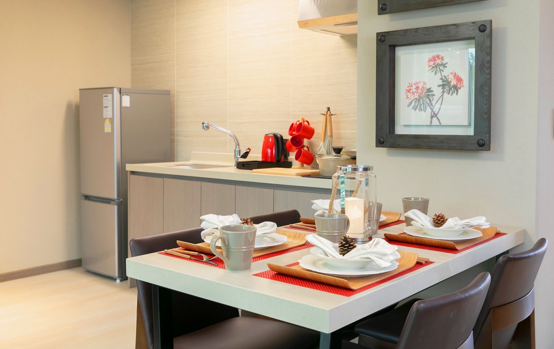 A modern kitchen with a refrigerator, sink, and a dining area set with plates, cups, and a candle.