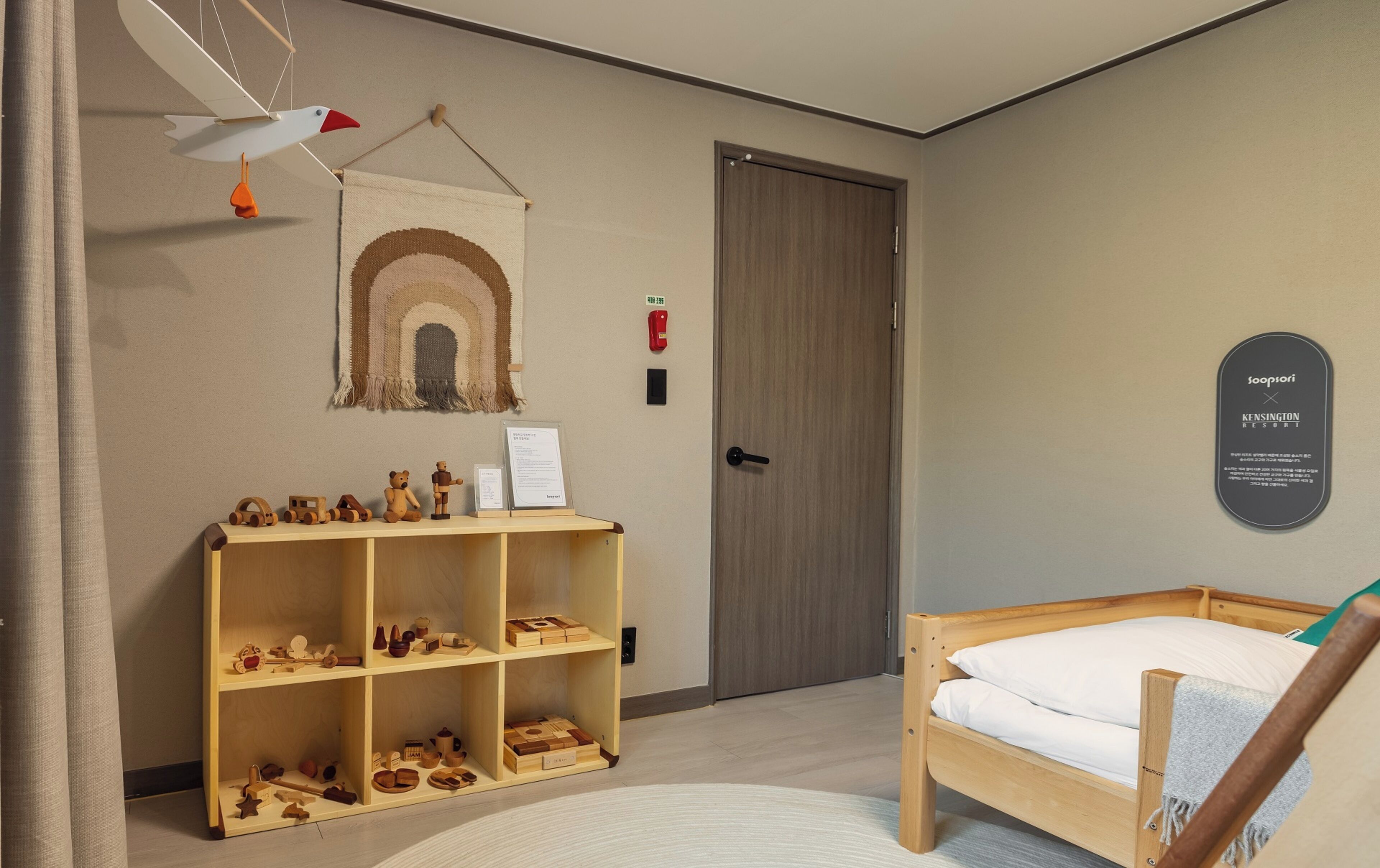 Una habitación con una cama de madera, un estante de madera con juguetes, un tapiz colgado en la pared y un cartel enmarcado.