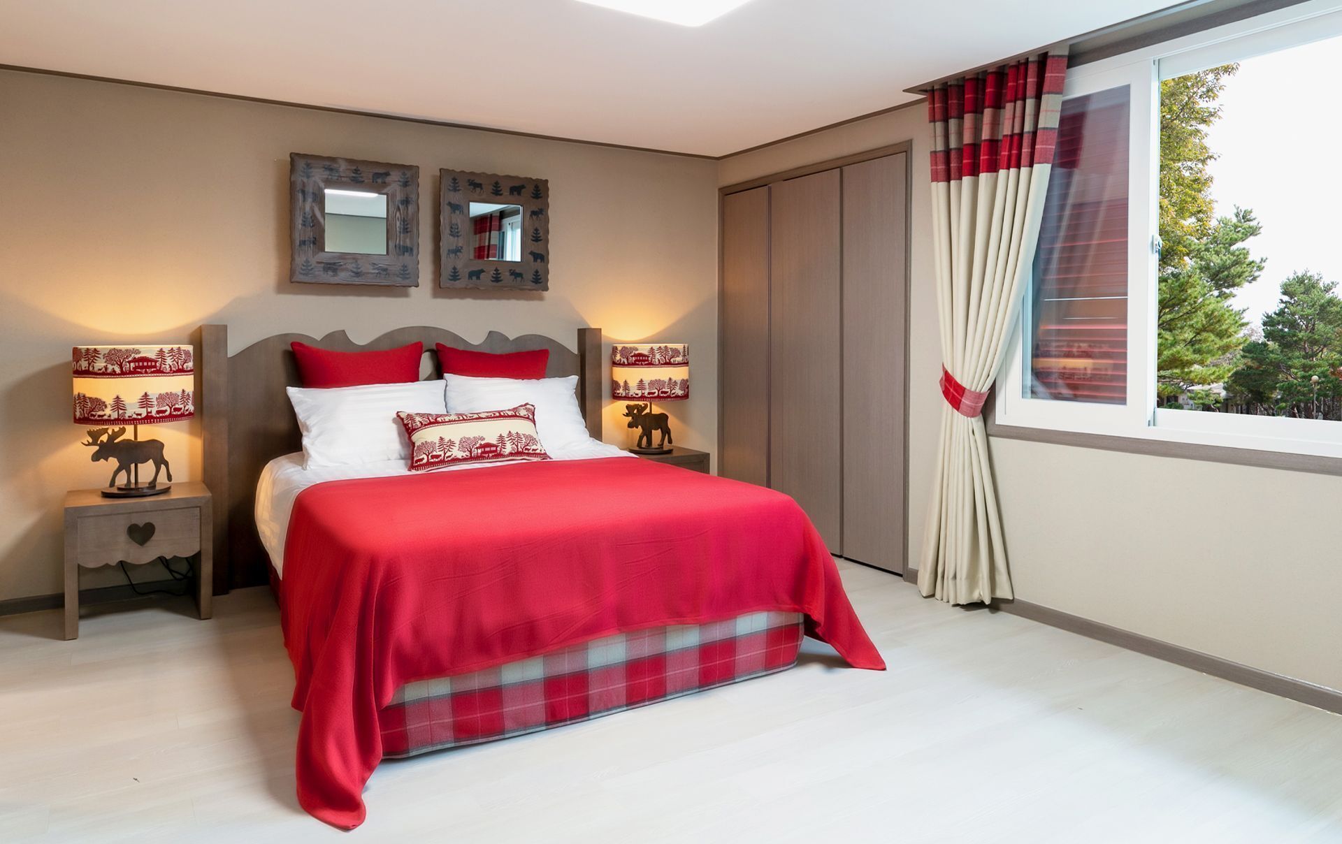 A bedroom with a large bed, two bedside tables with lamps, a mirror, and a window with curtains.