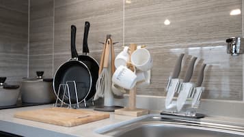 A kitchen with a sink, a wooden cutting board, a frying pan, a whisk, a mug holder, and a knife block.