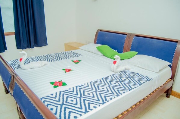 A neatly made bed with a patterned bedspread, pillows, and decorative swans. - 27 Cafe Zanzibar Airport Hotel (Zanzibar Town)