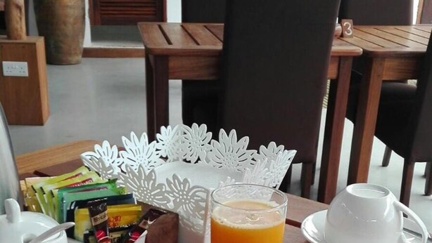 A breakfast table with a plate of watermelon and cucumber slices, a glass of orange juice, and a white teapot. - 27 Cafe Zanzibar Airport Hotel (Zanzibar Town)