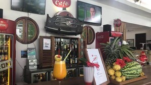 A bar area with a variety of liquor bottles, a sign for '27 Cafe', and a fruit display including pineapple and watermelon. - 27 Cafe Zanzibar Airport Hotel (Zanzibar Town)