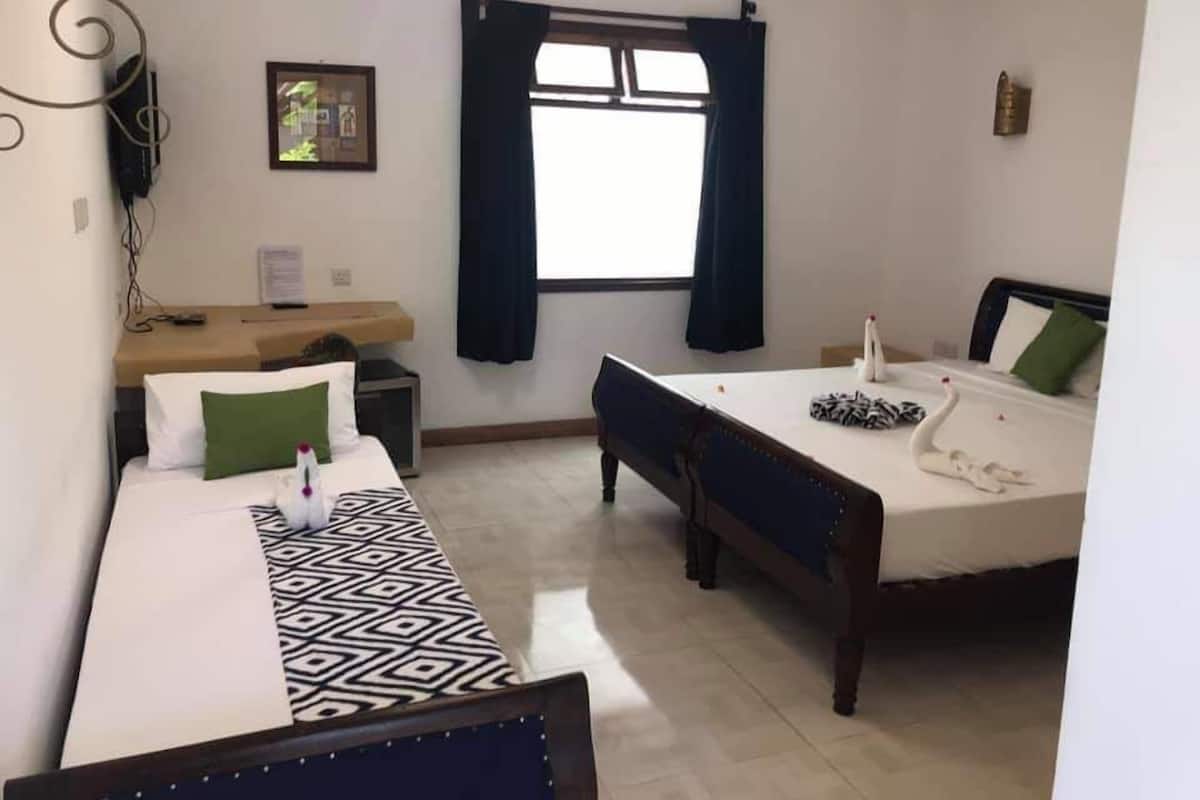 A hotel room with two beds, a desk, a chair, a window with curtains, and a wall-mounted air conditioner.