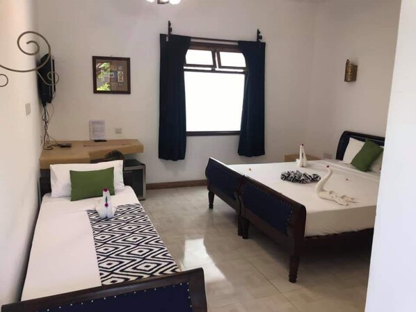 Habitación de hotel con dos camas, un escritorio, una silla, una ventana con cortinas y un aire acondicionado de pared.