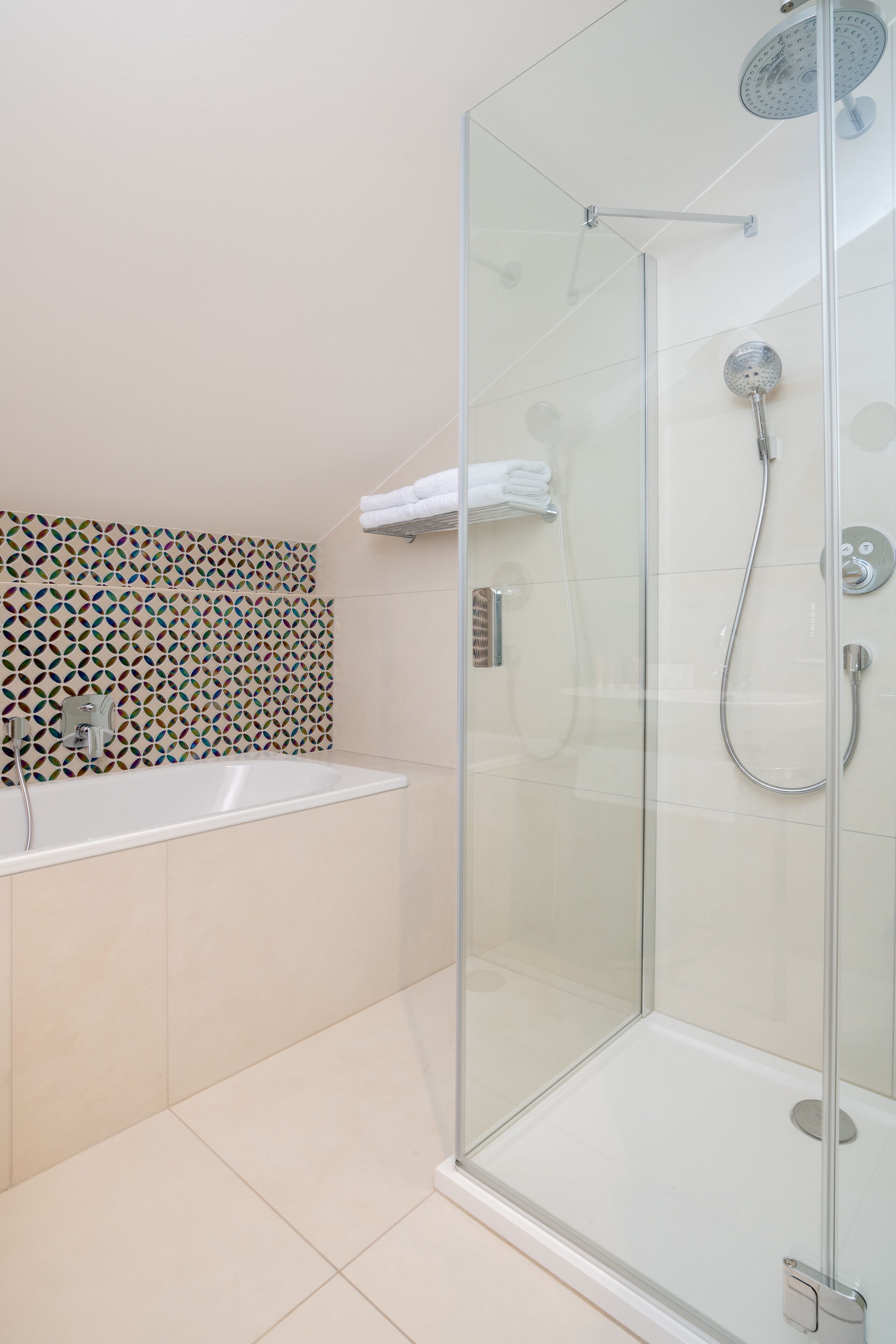 Een moderne badkamer met een douchecabine van glas, een wit wastafeltje en een betegelde spatwand.