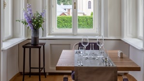 Ein Essbereich mit einem Tisch für vier Personen, einer Blumenvase und Blick auf ein Gebäude durch ein großes Fenster.