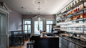 Eine Bar mit einer langen Theke, Hockern und Regalen voller Flaschen und Gläsern.