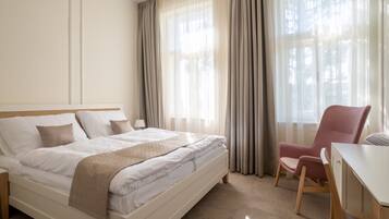 A hotel room with a bed, a desk, a chair, and a window with curtains.