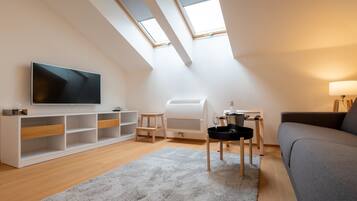 A modern loft apartment with a large TV, a built-in air conditioner, a cozy seating area, and skylights.